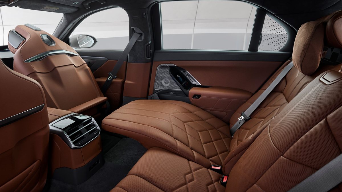 The rear seat of a BMW 7 Series fully reclined with the footrest extended, the ceiling screen stowed, in tan leather.