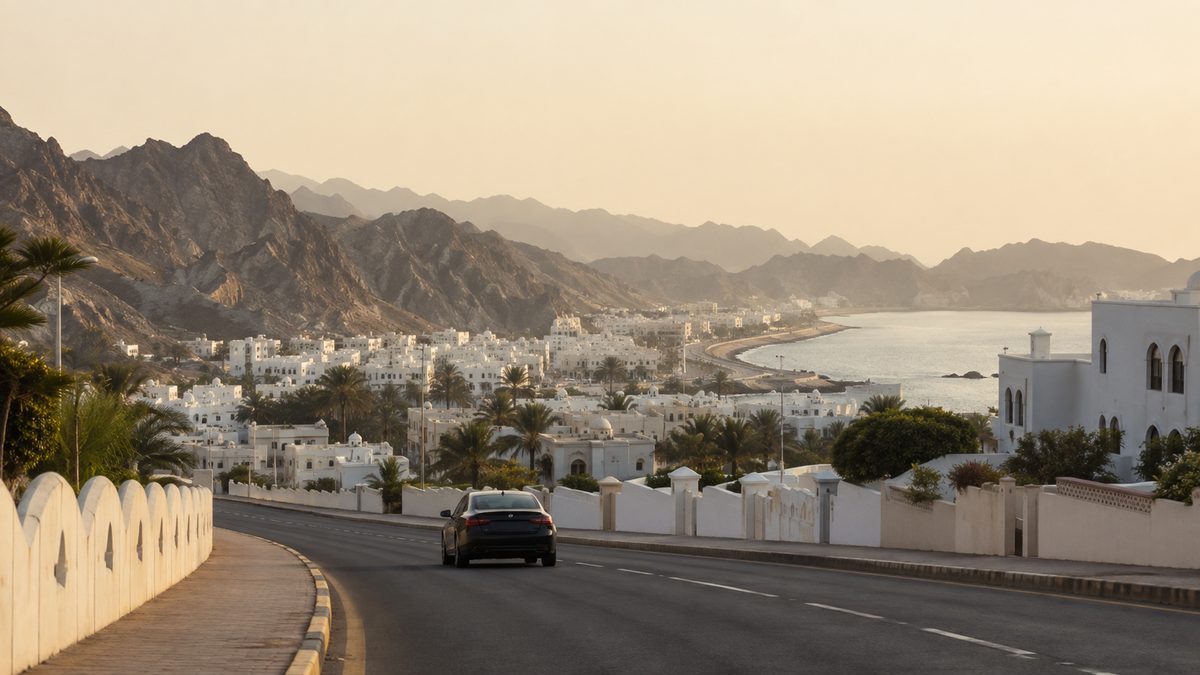 A road running through Muscat's low white buildings, between the mountains and the sea
